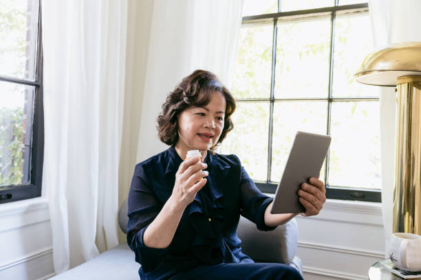 istock Woman holding pill bottle video conferences with doctor 1185470059