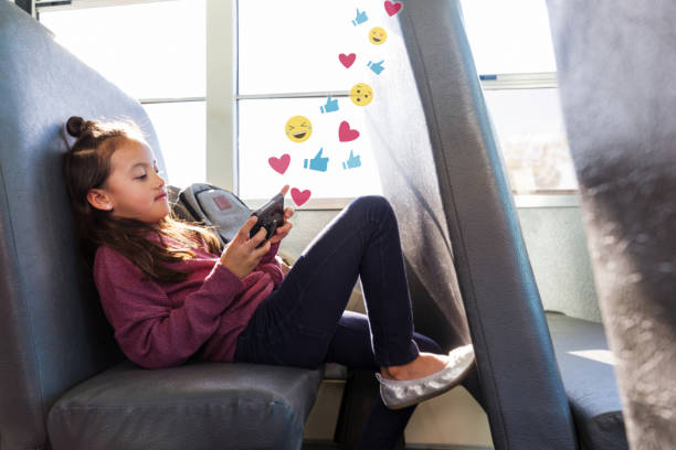 Preteen girl using social media while on school bus Young schoolgirl relaxes on the school bus. She is checking her social media account on her smartphone. Graphics of emojis, like buttons and heart symbols flow out from her smartphone. heart emoji phone stock pictures, royalty-free photos & images