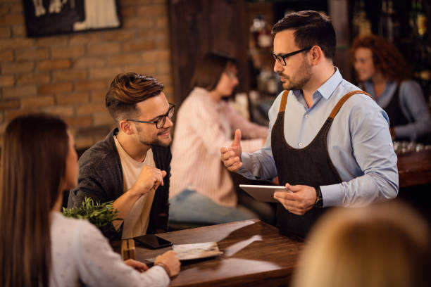 istock Waiter talking with a couple while using touchpad and taking their order in a pub. 1185470432