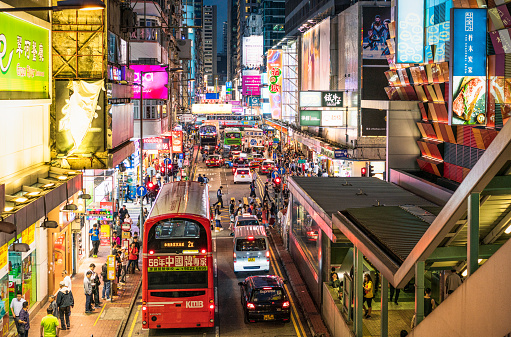 A high angle view of streets busy with pedestrians and traffic, as well as illumiated advertising signs in Mong Kok, Hong Kong.