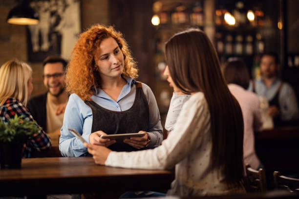 istock Young waitress with touchpad talking with female guest in a bar. 1185471967