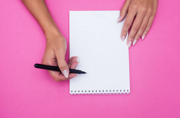 istock Notebook with pen holds female hands on a pink background. 1185471988