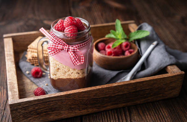 No-bake layered dessert with dark chocolate mousse, crushed cookies and raspberry cream cheese in glass jar No-bake layered dessert with dark chocolate mousse, crushed cookies and raspberry cream cheese in glass jar on rustic wooden background cake jar stock pictures, royalty-free photos & images