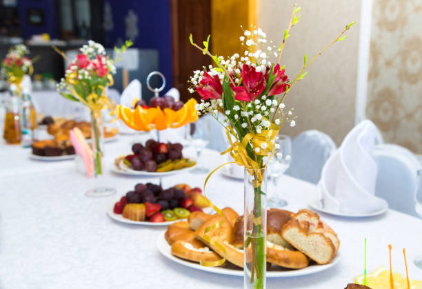 Beautiful table setting with a bouquet of flowers. White tablecloth with white napkins. Bright fruits and vegetables on the table. Wedding table. Holiday, Christmas, new year, birthday. Blurred background