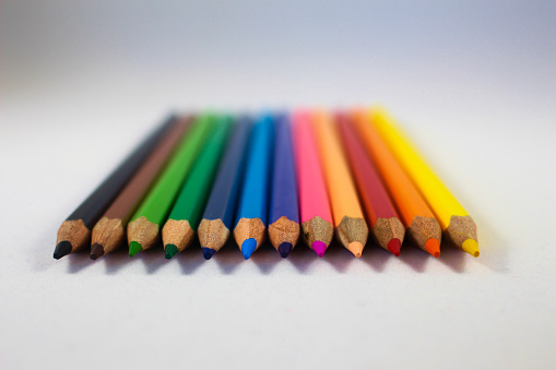 wooden colored pencils in a row on white paper background