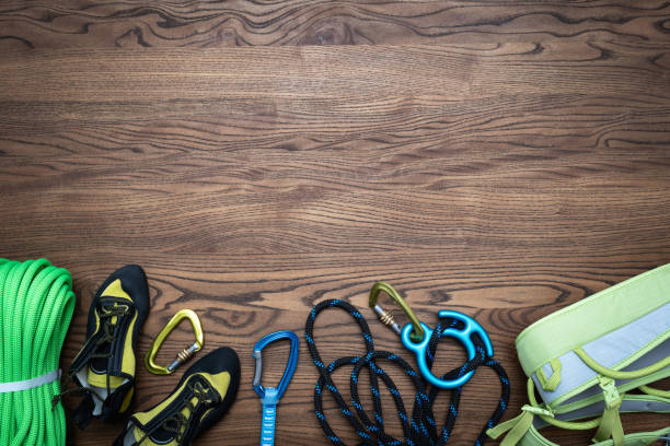 Top view of collection with climbing items, rope, quickdraw, carabiners, harness and shoes on wooden texture background with copy space