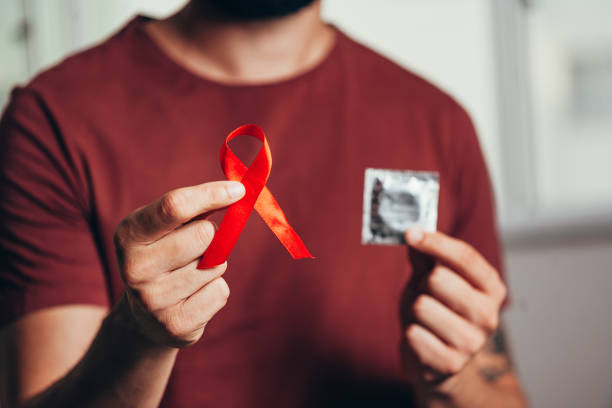 uomo in possesso di preservativo e nastro rosso per la consapevolezza della malattia da hiv, 1° dicembre giornata mondiale contro l'aids - aids foto e immagini stock