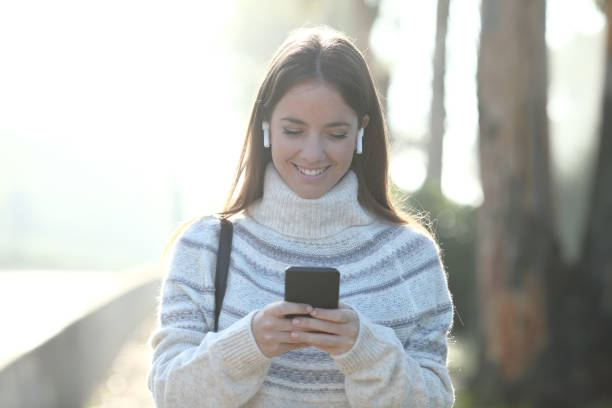 istock Happy woman in winter using mobile phone walking in a park 1185495403