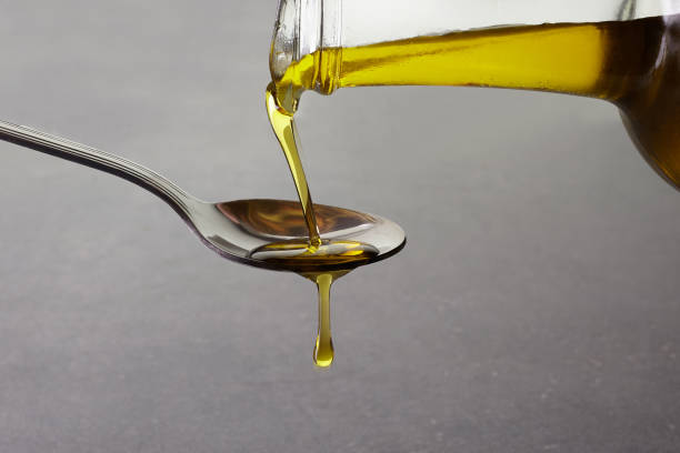pouring olive oil from glass bottle on grey background pouring olive oil from glass bottle on grey background. close up olive oil pouring antioxidant liquid stock pictures, royalty-free photos & images