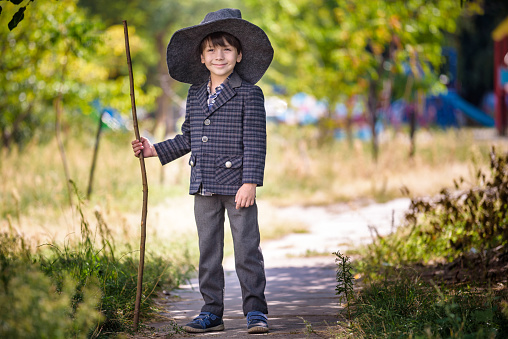 Toddler boy in pointed hat playing with magic wand outdoors. Little wizard. Halloween concept.