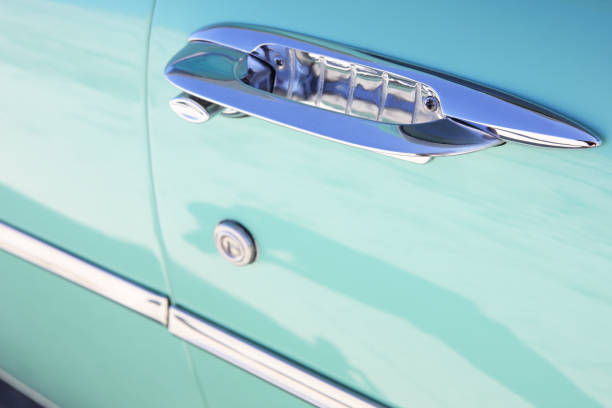 Antique car door handle in chrome on original 1957 teal factory color, close-up in horizontal composition, handle appearing diagonally in the upper right quadrant, key-lock below at mid-frame, and chrome side trim lower left quadrant.