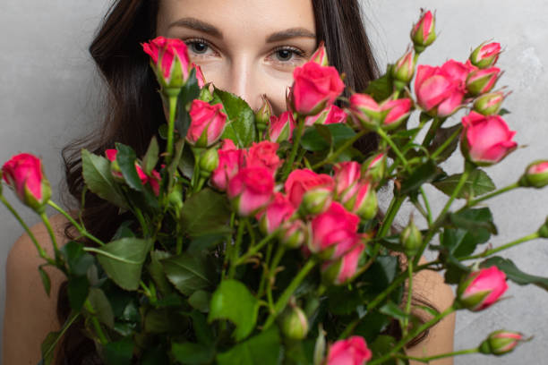 Close-up portrait of an attractive young woman in a summer dress holding a bouquet of roses looking at the camera, on a gray background stock photo
