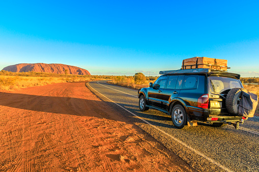 Uluru, Northern Territory, Australia - Aug 25, 2019: 4X4 vehicle on the road leading to Ayers Rock, Uluru-Kata Tjuta National Park at sunset. Majestic monolith in Australian outback, Central Australia
