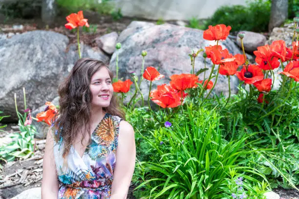 Vail town or village city in Colorado summer with happy woman young girl sitting by large big red poppy flowers in garden by rocks