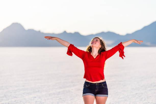 young happy woman with hands raised up on white bonneville salt flats near salt lake city, utah and mountain view during sunset - 12014 imagens e fotografias de stock