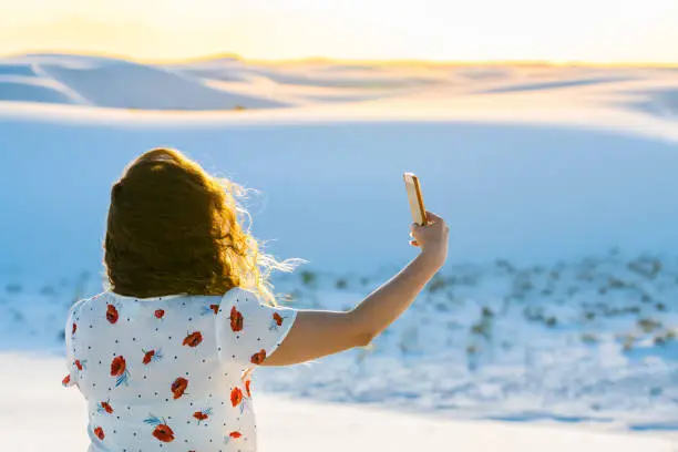 Woman closeup taking selfie picture in white sands dunes national monument in New Mexico using phone with wind