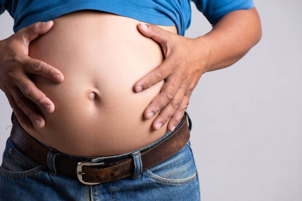 overweight or fat adult man hand holding belly stomach in very tight jeans on a gray background. healthcare, medicine concept. - loose weight imagens e fotografias de stock