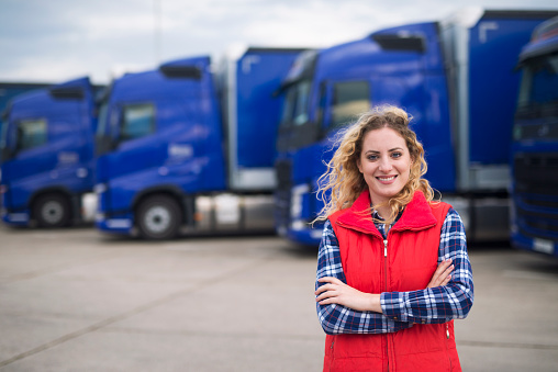 Portrait of female truck driver standing by trucks at truck stop.