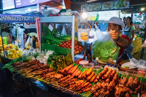 Thai woman selling street food at night market Bangkok, Thailand - March 2, 2018: Thai woman selling spicy grilling pork - traditional Thai food at night market, Khaosan road, Bangkok, Thailand. Street cooking is a tradition in Thailand. khao san road stock pictures, royalty-free photos & images