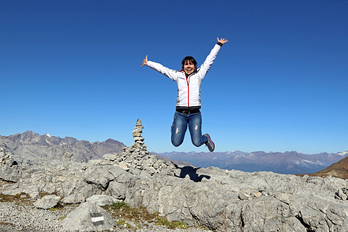 A young woman jumps into the air in the mountains laughing for joy.