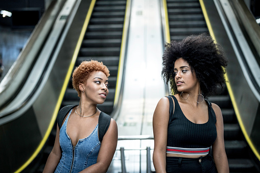 Two women standing in front of escalators in a subway station