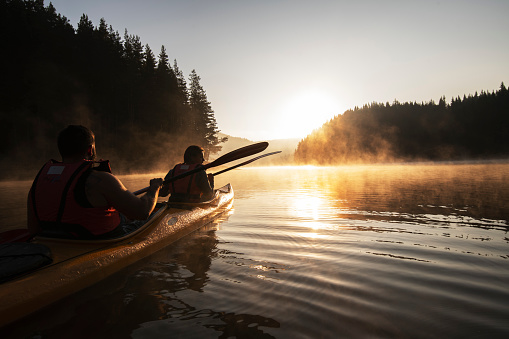 Young couple kayaking in nature before sunrise.