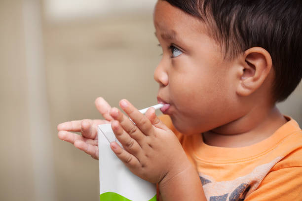 A 3 year old boy that has learned how to hold a juice box on his own and drink from a straw. stock photo