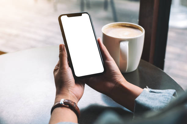 uma mulher que prende o telefone móvel preto com tela em branco com copo de café na tabela de madeira - smart phone telephone human hand mobile phone - fotografias e filmes do acervo