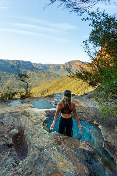 femme dans les piscines naturelles de plongeon à la fin du canyon avec la vue de montagne - blue mountains national park photos et images de collection