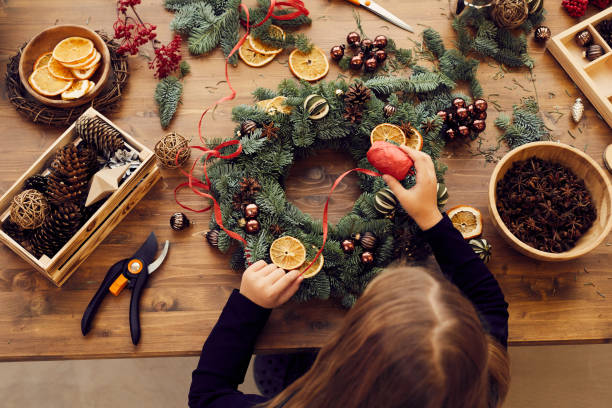 vue d'angle élevé de la femme occupée restant au bureau et utilisant le ruban décoratif tout en faisant la couronne de noel - preparation photos et images de collection