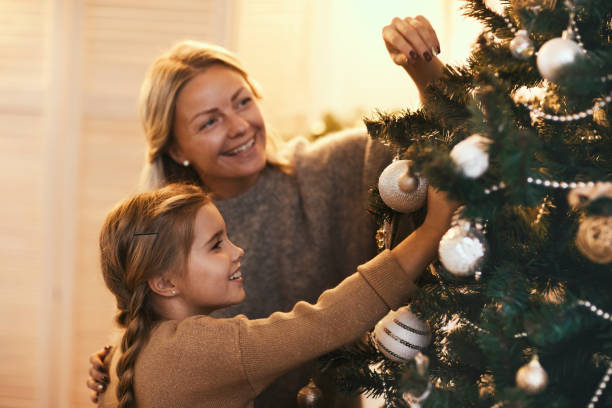istock Happy beautiful mother and daughter decorating coniferous tree with baubles while preparing home for Christmas 1185568249