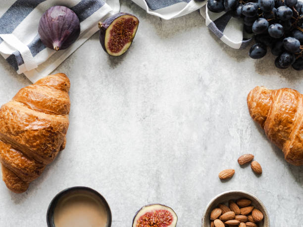 Breakfast frame with croissants, figs, almonds and espresso coffee on grey background, top view, copy space