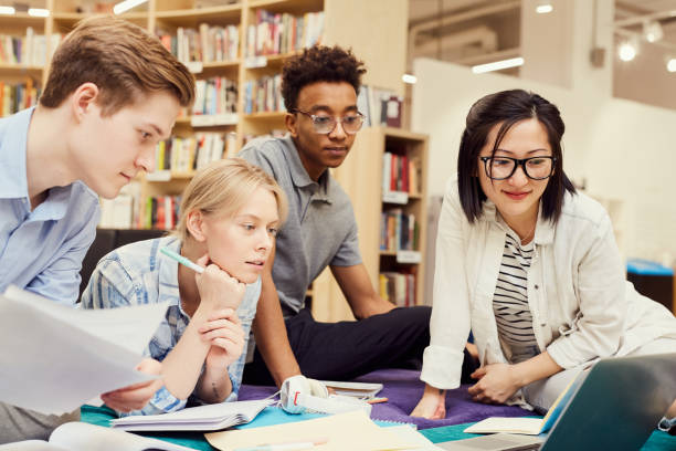 istock Group of thoughtful young multi-ethnic students focused on joint project sitting among workbooks and devices in library and looking at laptop screen 1185581958