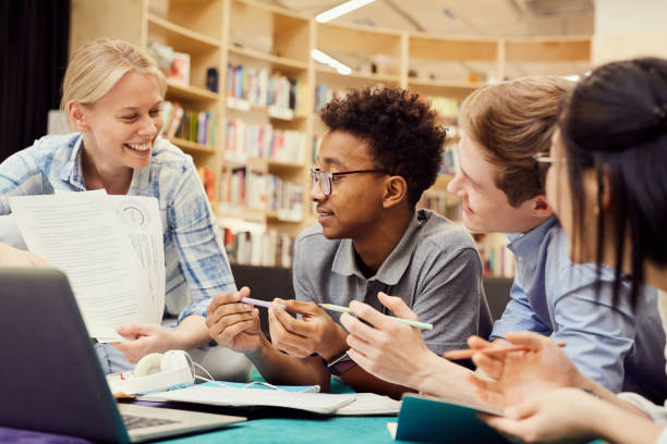 istock Group of cheerful young multi-ethnic university students sitting in campus lobby and exchanging project ideas 1185581972