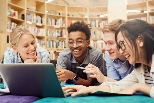 positiv aufgeregt multiethnische studenten in lässiger kleidung auf dem boden in campus bibliothek liegen und lachen, während neugierige video auf laptop zu sehen - school library stock-fotos und bilder