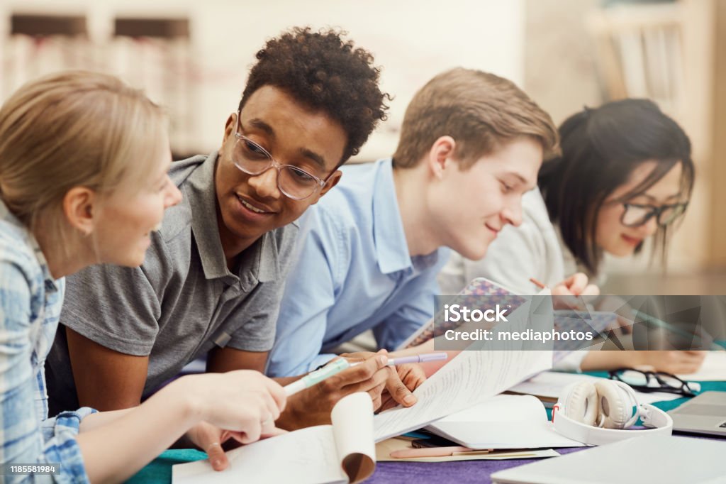 Content young multi-ethnic students lying in row and discussing hometask while viewing notes in workbooks Students discussing hometask Teenager Stock Photo