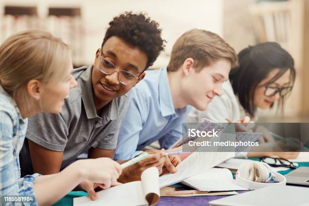 Content Young Multiethnic Students Lying In Row And Discussing Hometask While Viewing Notes In Workbooks Stock Photo - Download Image Now