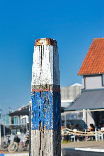 wooden pole with old chipped blue and white paint for fastening boats at oudeschild harbor in front of blue background - oudeschild imagens e fotografias de stock