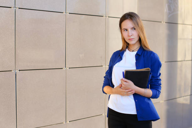 istock Cute student girl stands and looks to side, holds day planner, Students' work, notebook and pen 1185590675