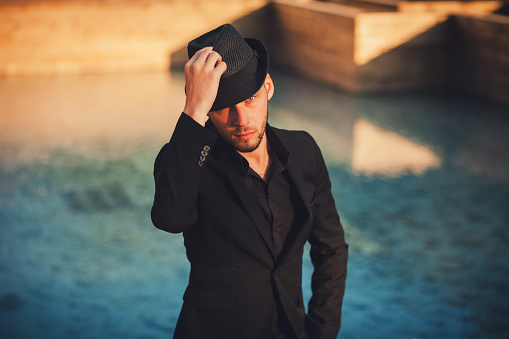 handsome man in a black suit and hat posing outdoors. Fashion & Style