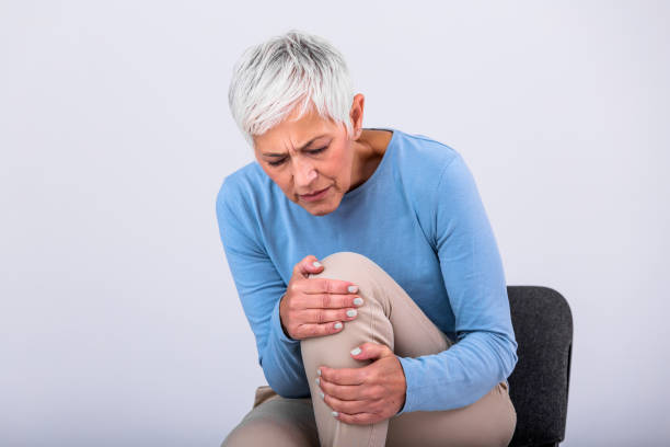 senior woman holding the knee with pain. old age, health problem and people concept - senior woman suffering from pain in leg at home. elderly woman suffering from pain in knee at home - old senior adult women tired imagens e fotografias de stock