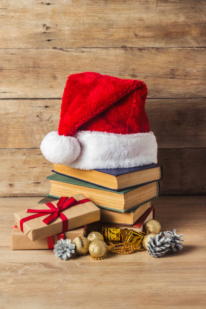 istock A stack of books, Santa Claus's cap, an alarm clock, cones, Christmas-tree decorations, gift boxes on a wooden background. Concept of New Year and Merry Christmas. 1185601142