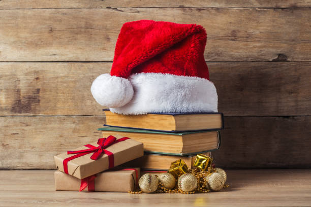istock A stack of books, Santa Claus's cap, Christmas-tree decorations, gift boxes on a wooden background. Concept of New Year and Merry Christmas. 1185603476