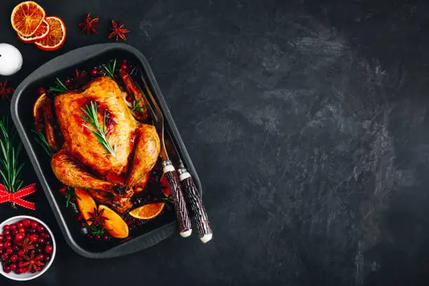Roasted chicken or turkey with spices, oranges and cranberries for Christmas or Thanksgiving on dark concrete stone background.