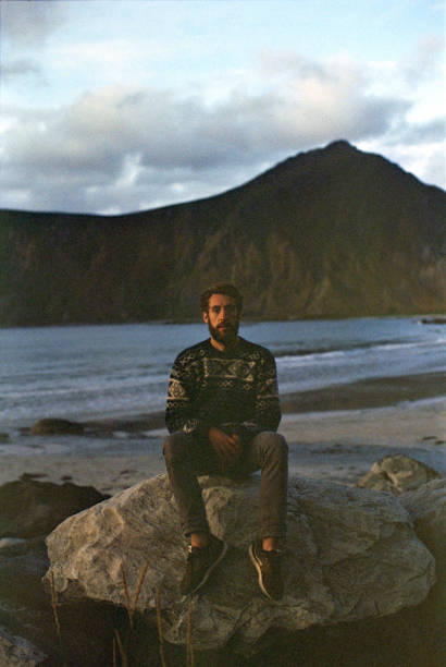 istock Man sitting on rock on beach on Lofoten island 1185615224