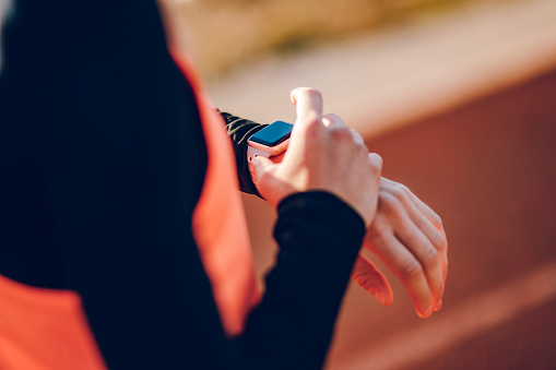 Close-up of young woman setting and checking smart watch on a race track.