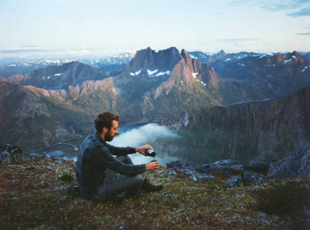 Young Caucasian man  drinking tea from thermos with view in mountains on Senja Island