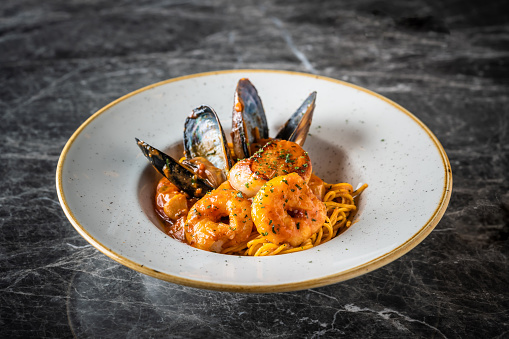 Pasta with Clams, mussels, calamari, shrimps, and cherry tomatoes in marinara sauce on white background