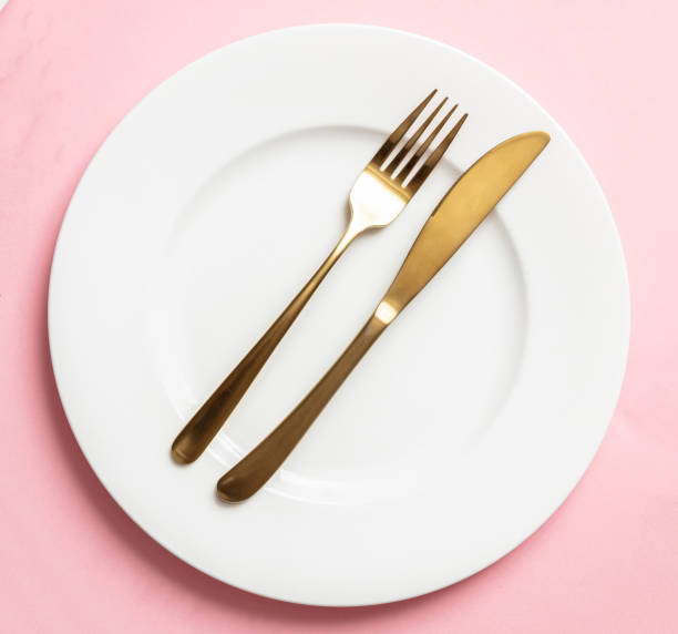 istock Gold cutlery and dishes set against pink background, formal place setting 1185628111