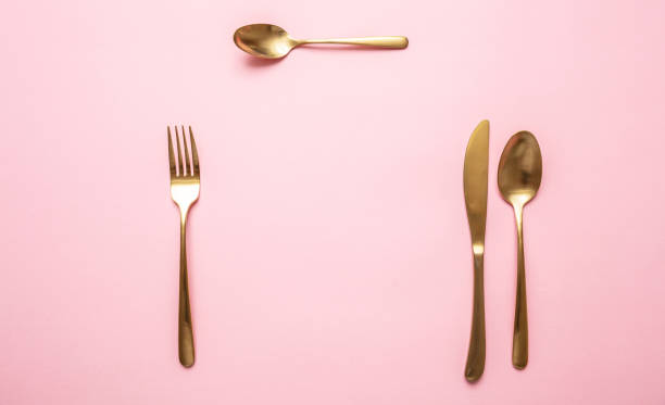 istock Gold cutlery set against pink background, formal place setting 1185628115